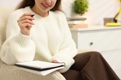 Photo of Woman with planner in armchair at home, closeup