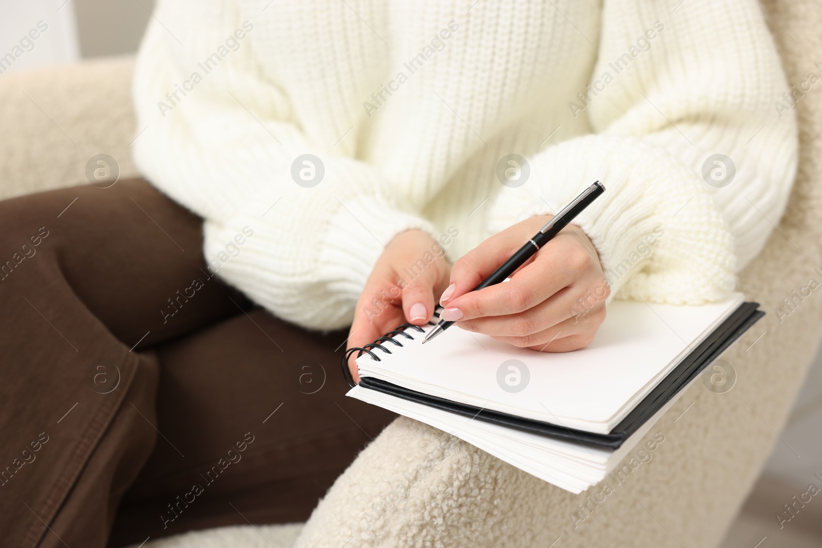 Woman writing in planner on armchair indoors, closeup Photo of Woman writing in planner on armchair indoors, closeup