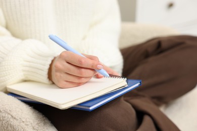 Photo of Woman writing in planner on armchair indoors, closeup