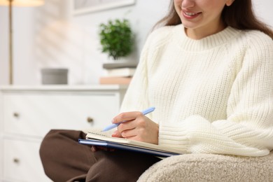 Photo of Woman writing in planner on armchair indoors, closeup. Space for text