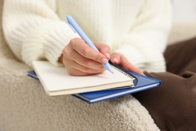 Photo of Woman writing in planner on armchair indoors, closeup