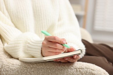 Photo of Woman writing in planner on armchair indoors, closeup