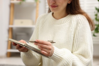 Photo of Woman writing in planner at home, closeup