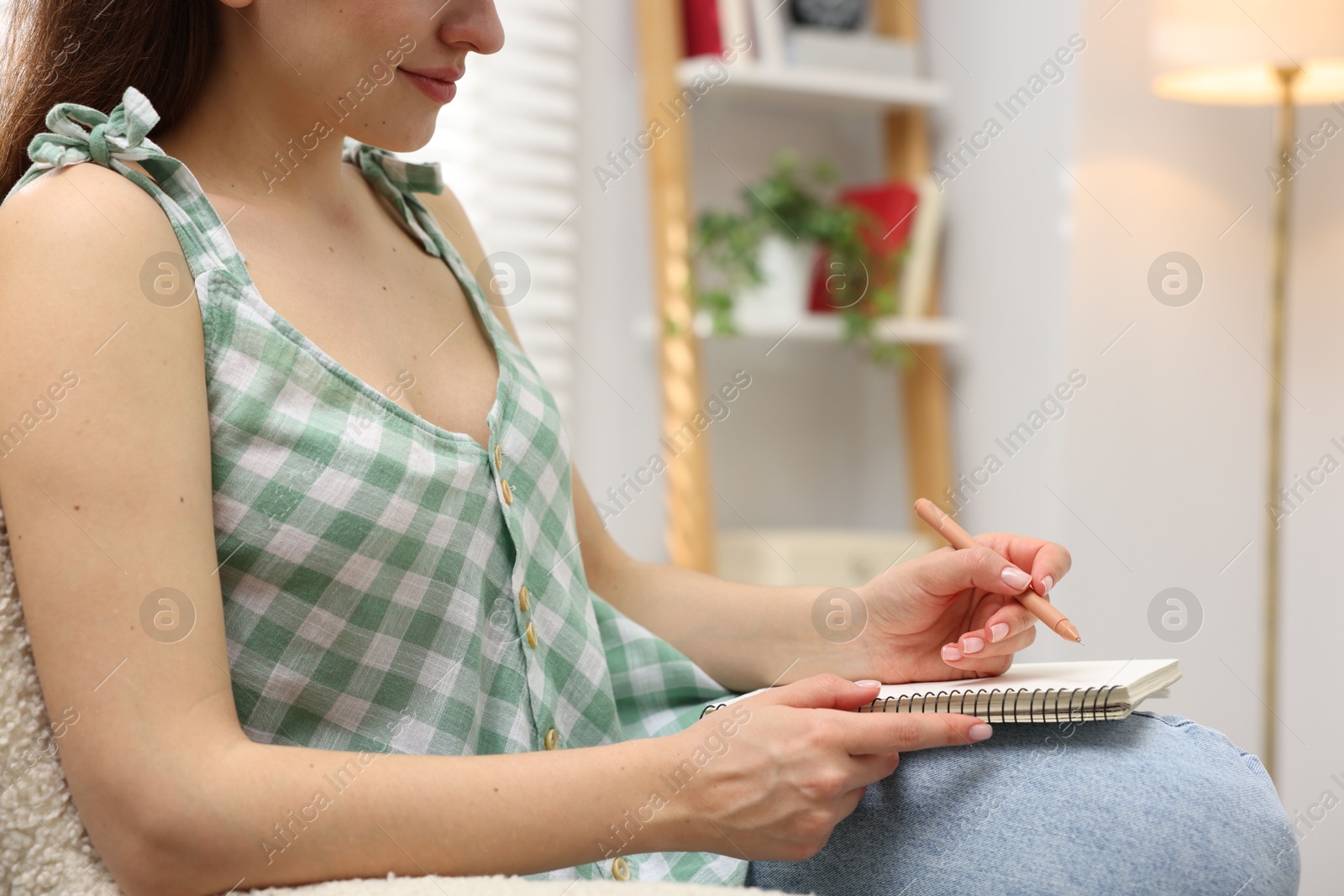 Woman writing in planner on armchair indoors, closeup Photo of Woman writing in planner on armchair indoors, closeup
