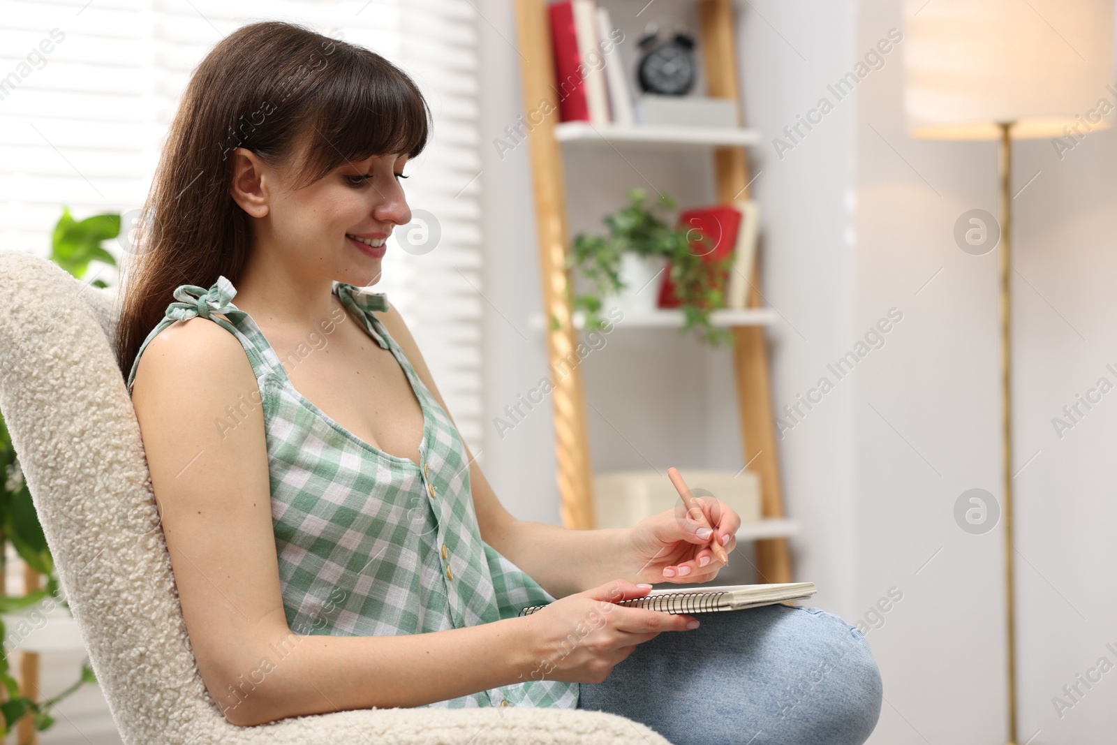 Woman writing in planner on armchair indoors. Space for text Photo of Woman writing in planner on armchair indoors. Space for text