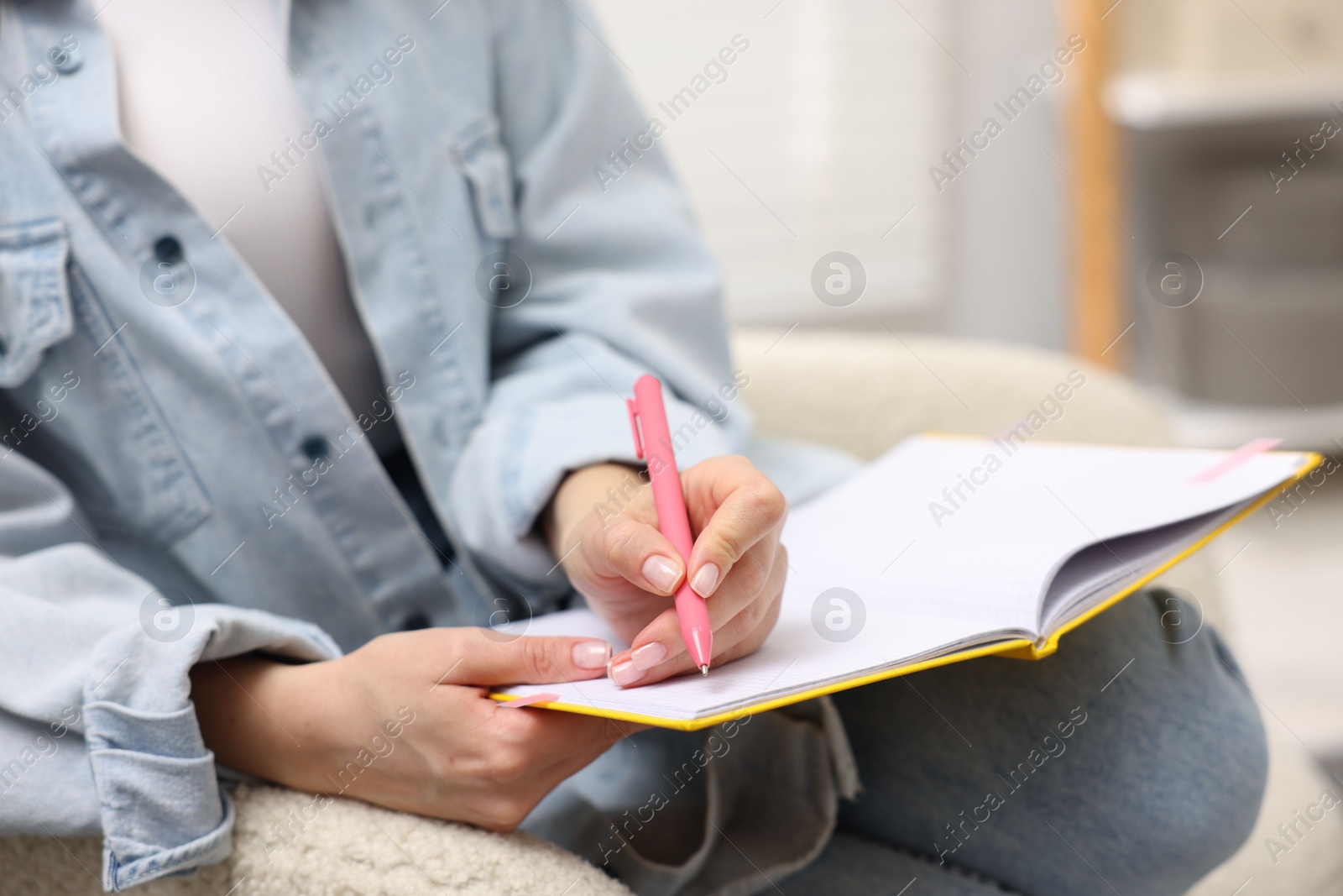 Woman writing in planner on armchair indoors, closeup Photo of Woman writing in planner on armchair indoors, closeup