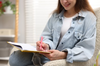 Photo of Woman writing in planner on armchair indoors, closeup. Space for text