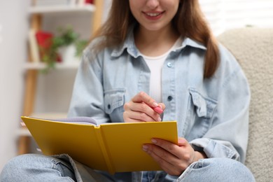 Photo of Woman writing in planner on armchair indoors, closeup