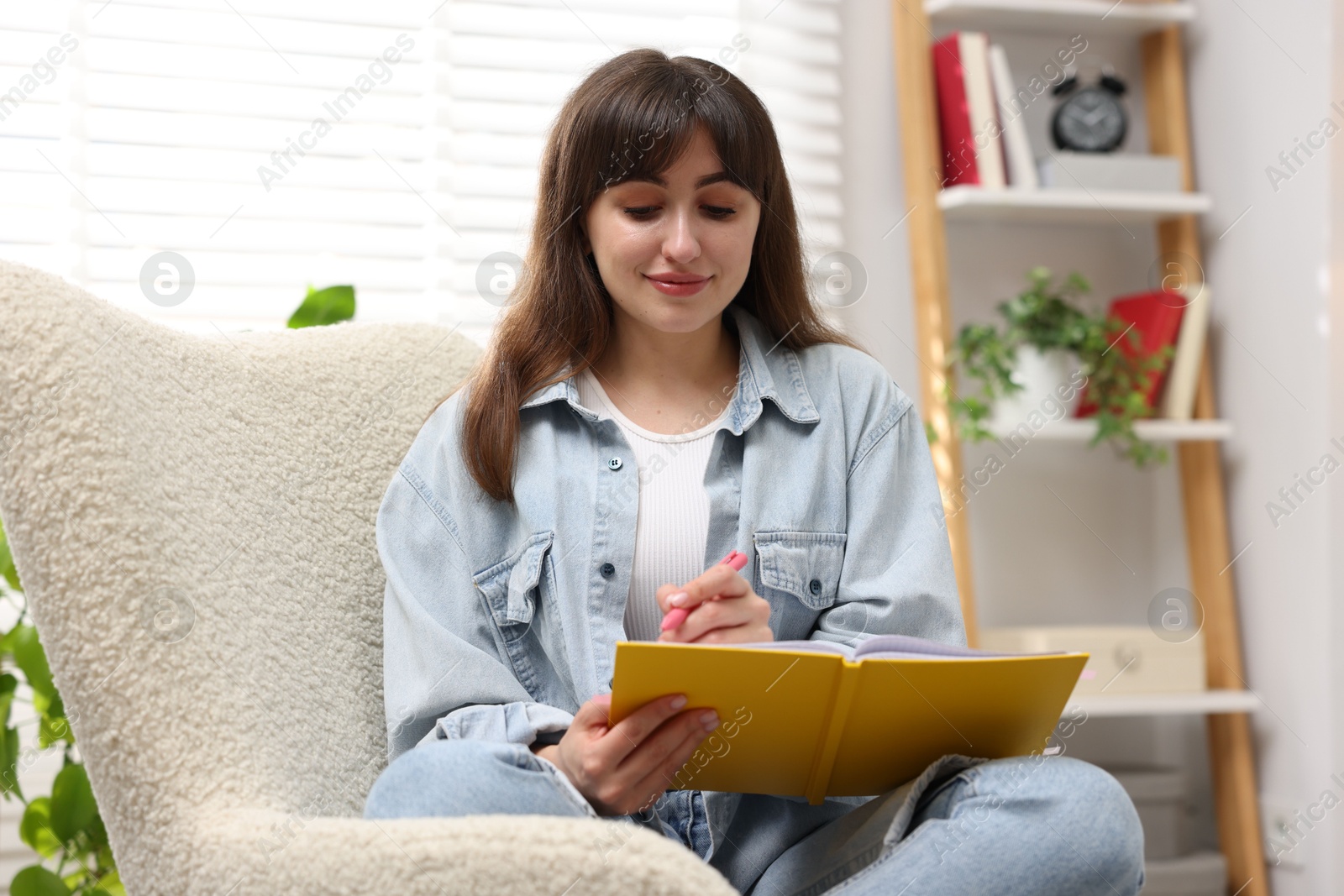Woman writing in planner on armchair indoors Photo of Woman writing in planner on armchair indoors
