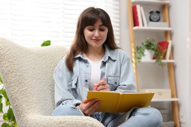 Photo of Woman writing in planner on armchair indoors