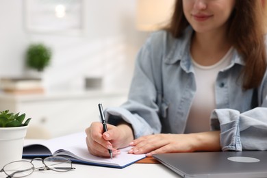 Photo of Woman writing in planner at white desk indoors, closeup. Space for text