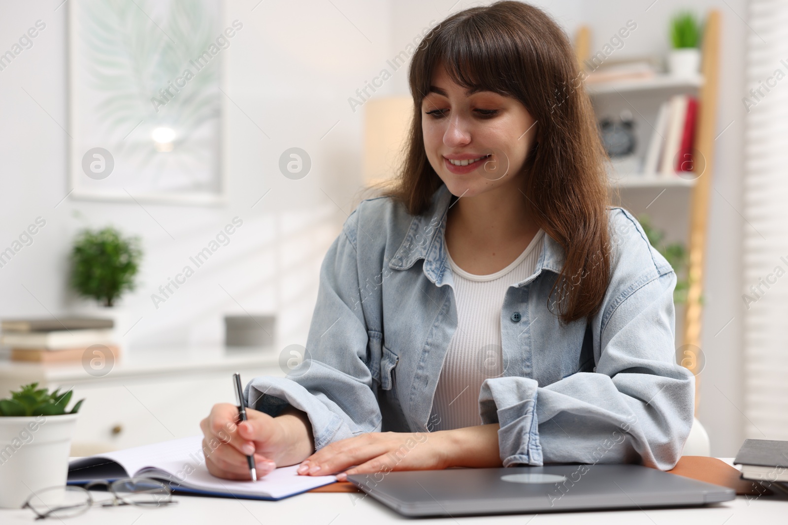 Photo of Woman with planner and laptop at white desk indoors. Space for text
