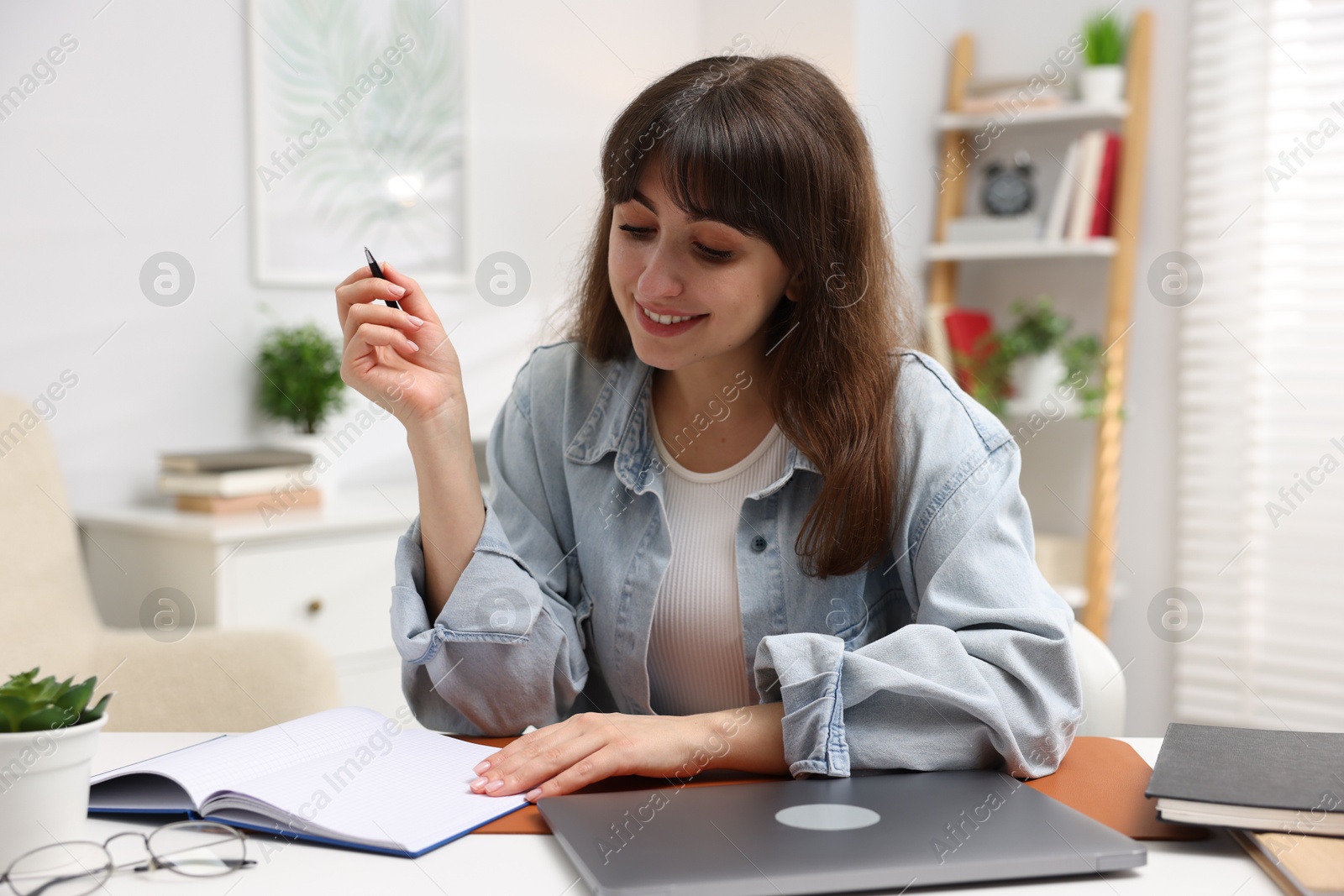 Photo of Woman with planner and laptop at white desk indoors