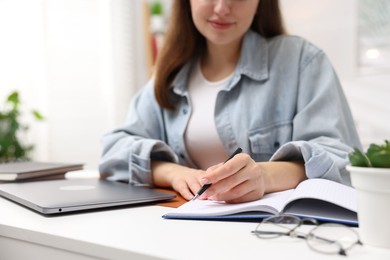Photo of Woman with planner and laptop at white desk indoors, closeup