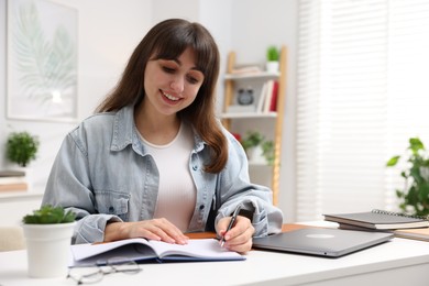 Photo of Woman with planner and laptop at white desk indoors. Space for text