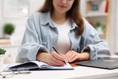 Photo of Woman with planner and laptop at white desk indoors, closeup