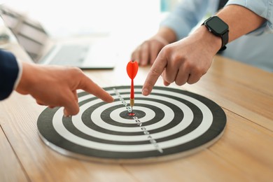 Photo of Men pointing at dartboard at wooden table indoors, closeup