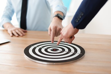 Photo of Men pointing at dartboard at wooden table indoors, closeup