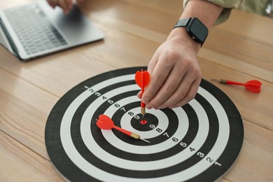 Photo of Man with dart aiming at dartboard while working on laptop indoors, closeup