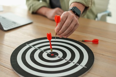 Photo of Man with dart aiming at dartboard while working indoors, closeup