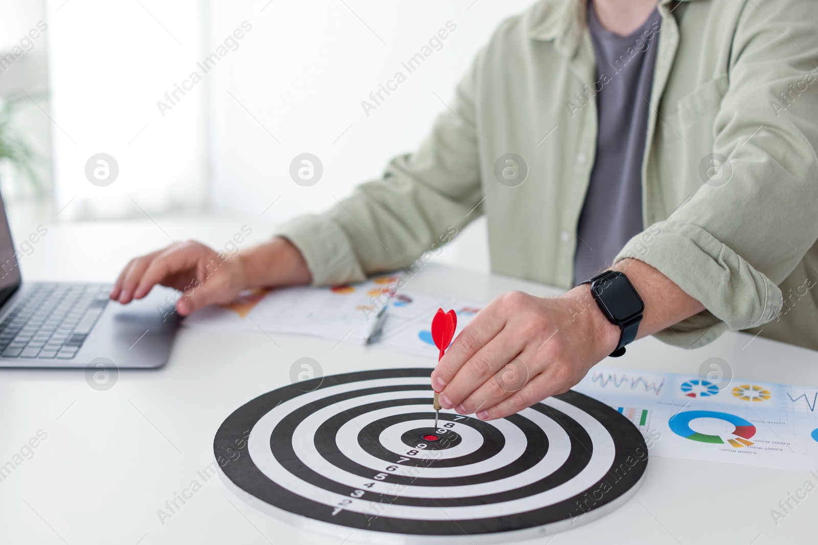 Photo of Man with dart aiming at dartboard while working indoors, closeup
