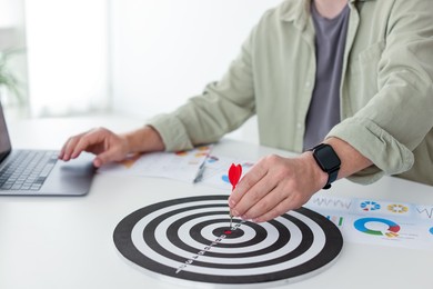 Photo of Man with dart aiming at dartboard while working indoors, closeup