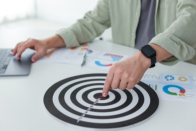 Photo of Man pointing at dartboard at white table indoors, closeup