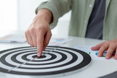 Photo of Man pointing at dartboard at white table indoors, closeup