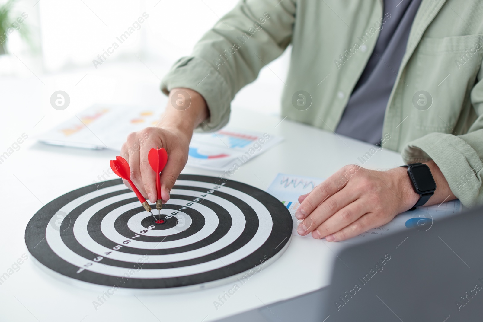 Photo of Man with dart aiming at dartboard indoors, closeup