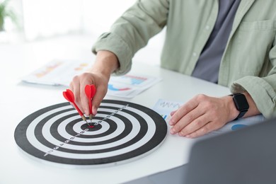 Photo of Man with dart aiming at dartboard indoors, closeup