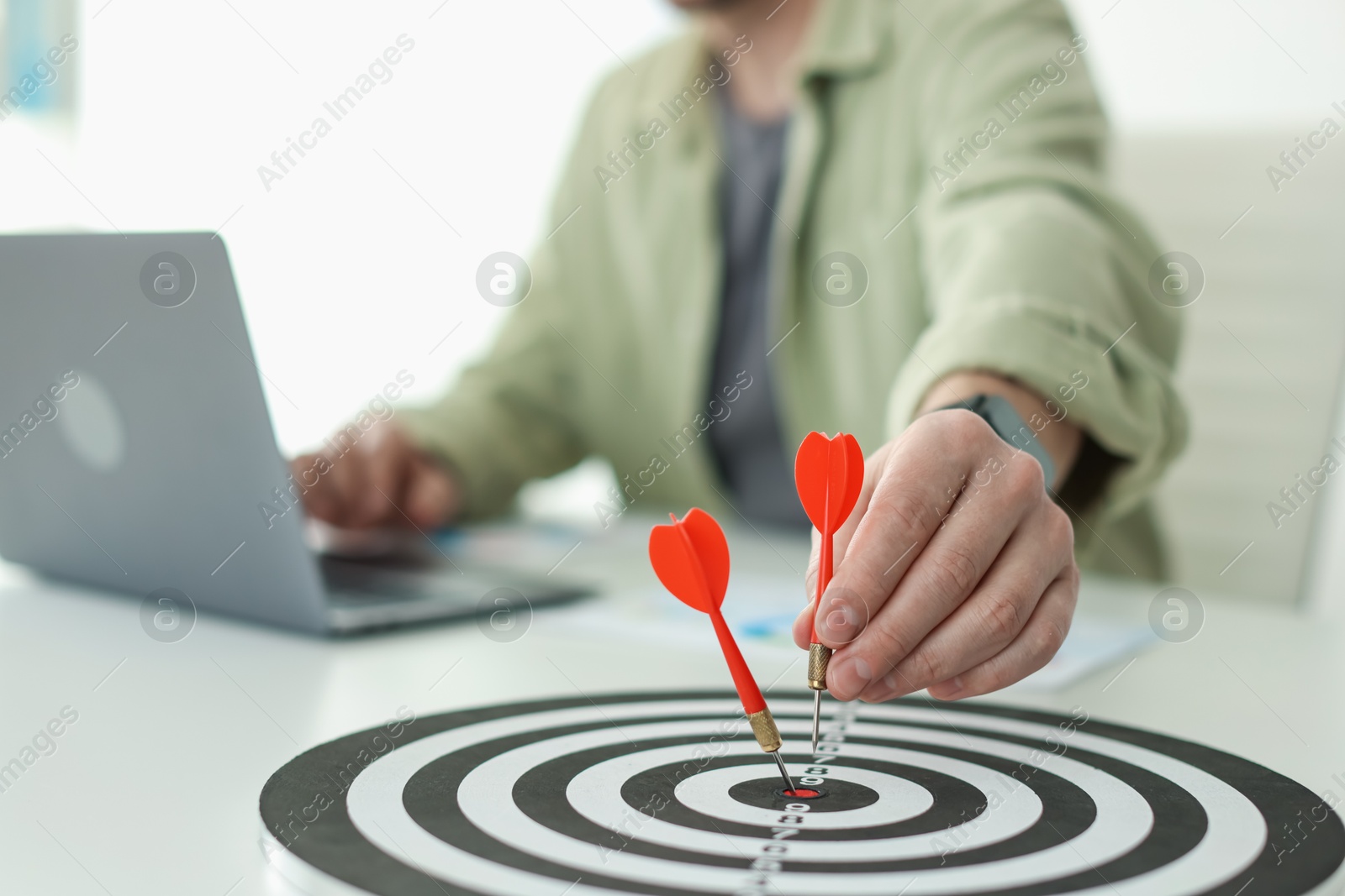 Photo of Man with dart aiming at dartboard while working indoors, closeup