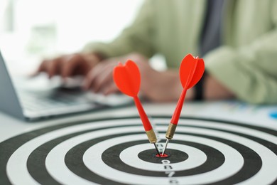 Photo of Man working on laptop at table, focus on dartboard with arrows indoors
