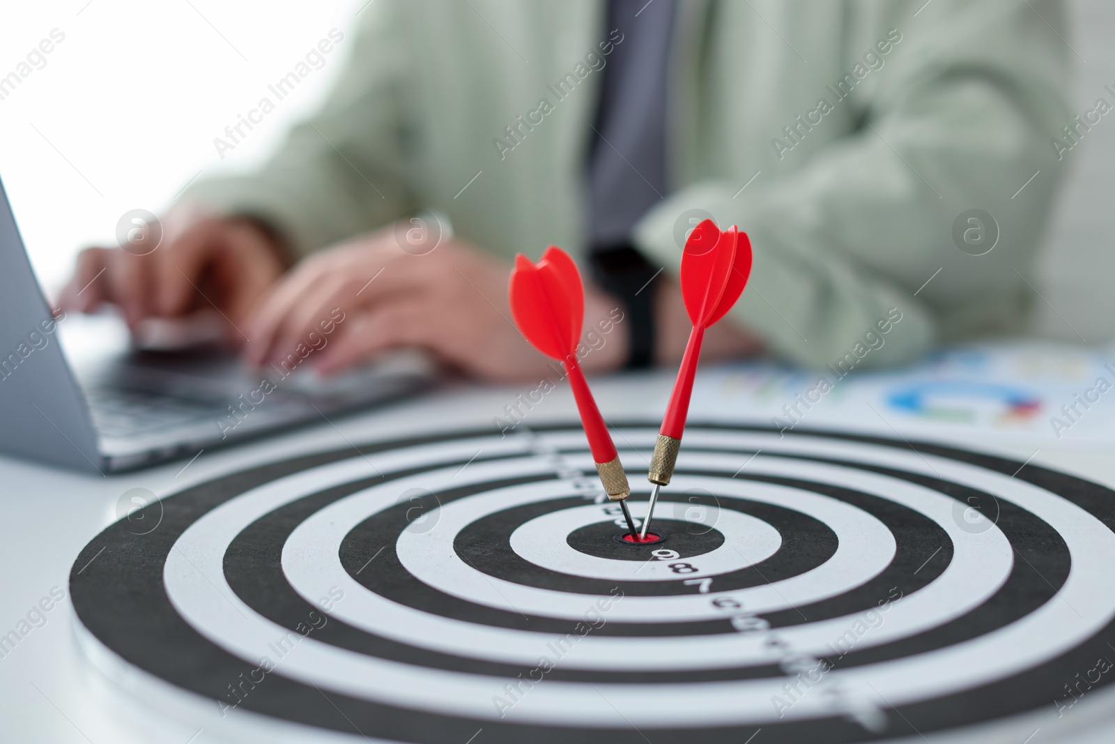 Photo of Man working on laptop at table, focus on dartboard with arrows indoors