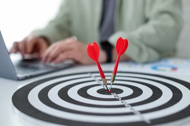 Photo of Man working on laptop at table, focus on dartboard with arrows indoors