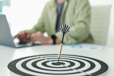 Photo of Man working on laptop at table, focus on dartboard with arrow indoors