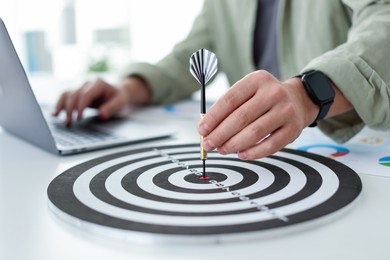 Photo of Man with dart aiming at dartboard while working indoors, closeup