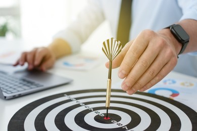 Photo of Man with dart aiming at dartboard while working indoors, closeup