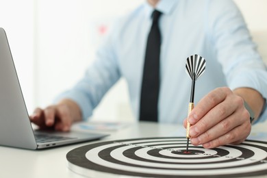 Photo of Man with dart aiming at dartboard while working indoors, closeup