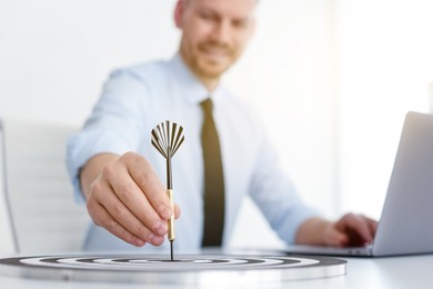 Photo of Man with dart aiming at dartboard while working indoors, selective focus
