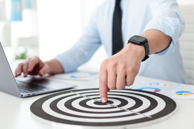 Photo of Man pointing at dartboard while working at white table indoors, closeup