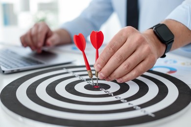 Photo of Man with dart aiming at dartboard while working indoors, closeup