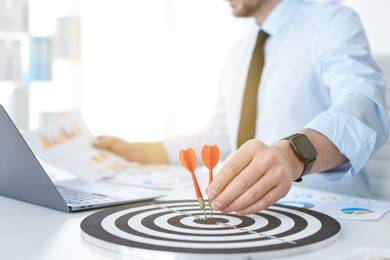 Photo of Man with dart aiming at dartboard while working indoors, closeup