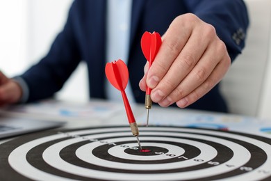 Photo of Man with dart aiming at dartboard while working indoors, closeup