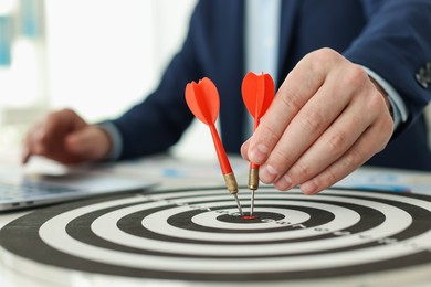 Photo of Man with dart aiming at dartboard while working indoors, closeup