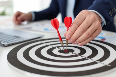 Photo of Man with dart aiming at dartboard while working indoors, closeup
