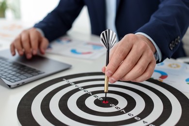 Photo of Man with dart aiming at dartboard while working indoors, closeup