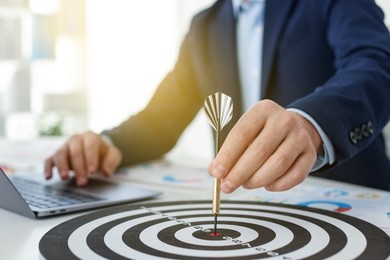 Photo of Man with dart aiming at dartboard while working indoors, closeup