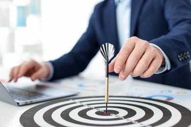 Photo of Man with dart aiming at dartboard while working indoors, closeup