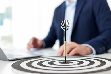 Photo of Man working on laptop at table, focus on dartboard with arrow indoors