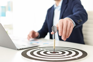 Photo of Man working on laptop at table, focus on dartboard with arrow indoors